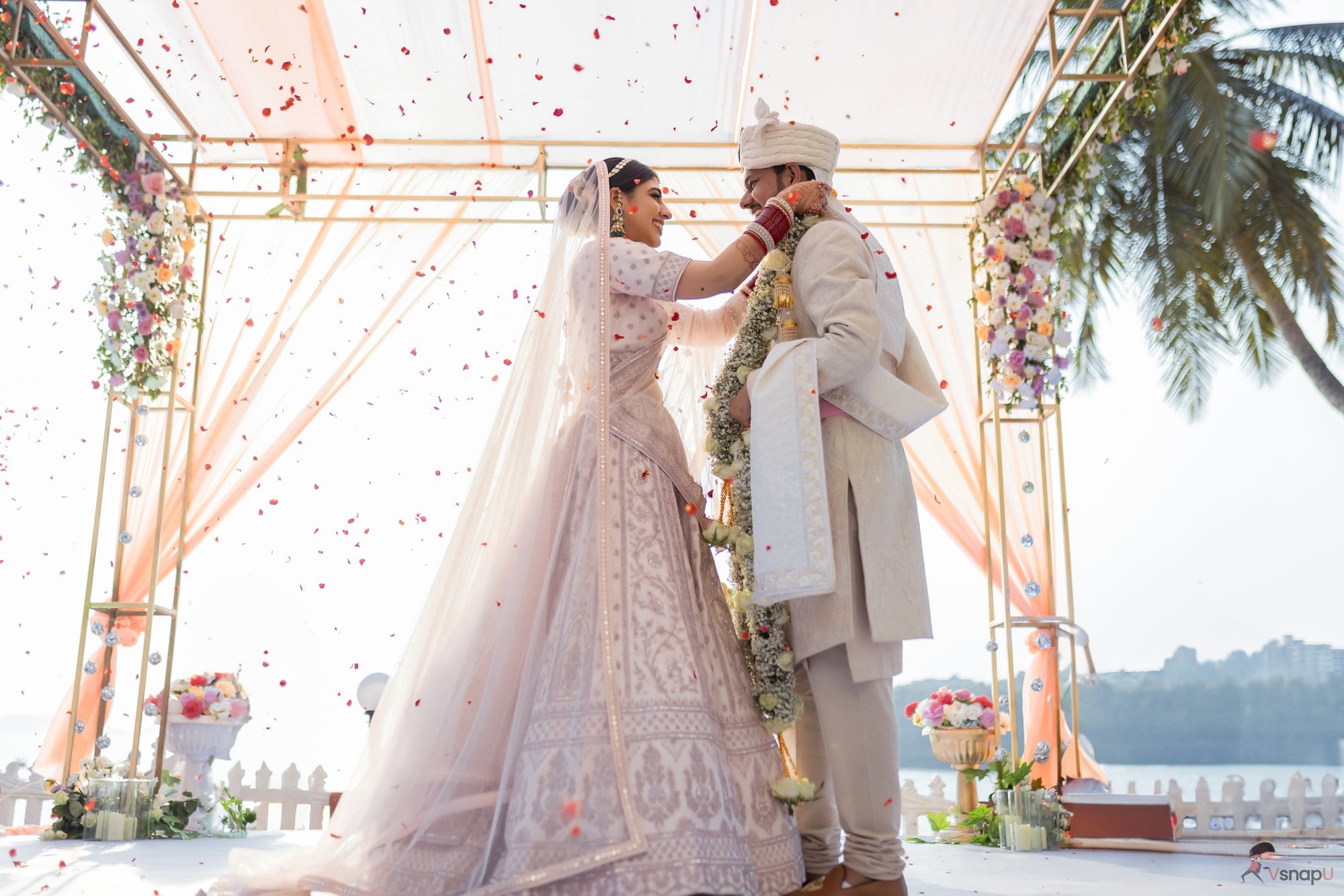 The bride gracefully puts the varmala on the groom amidst a floral wedding setup.