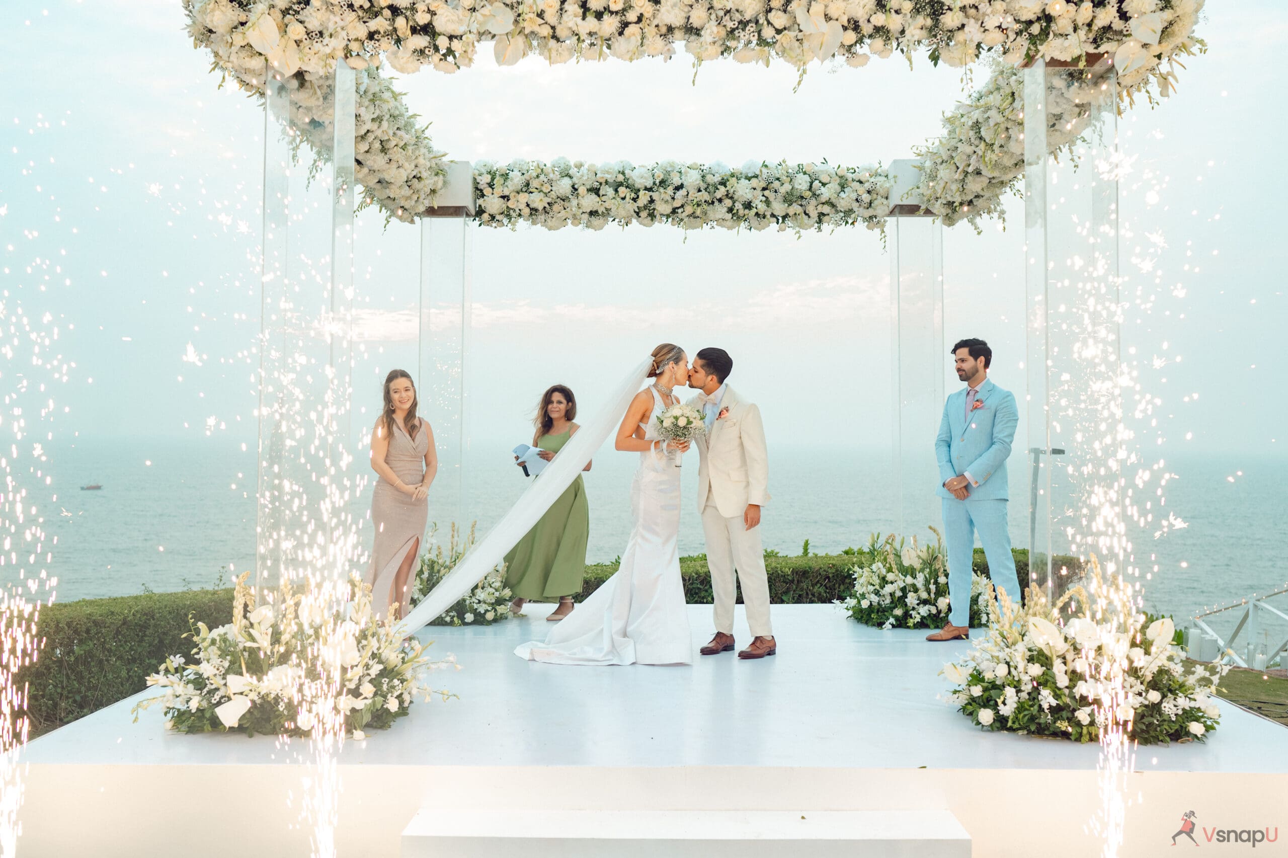 The couple shares an intimate moment, kissing under a canopy of flowers.