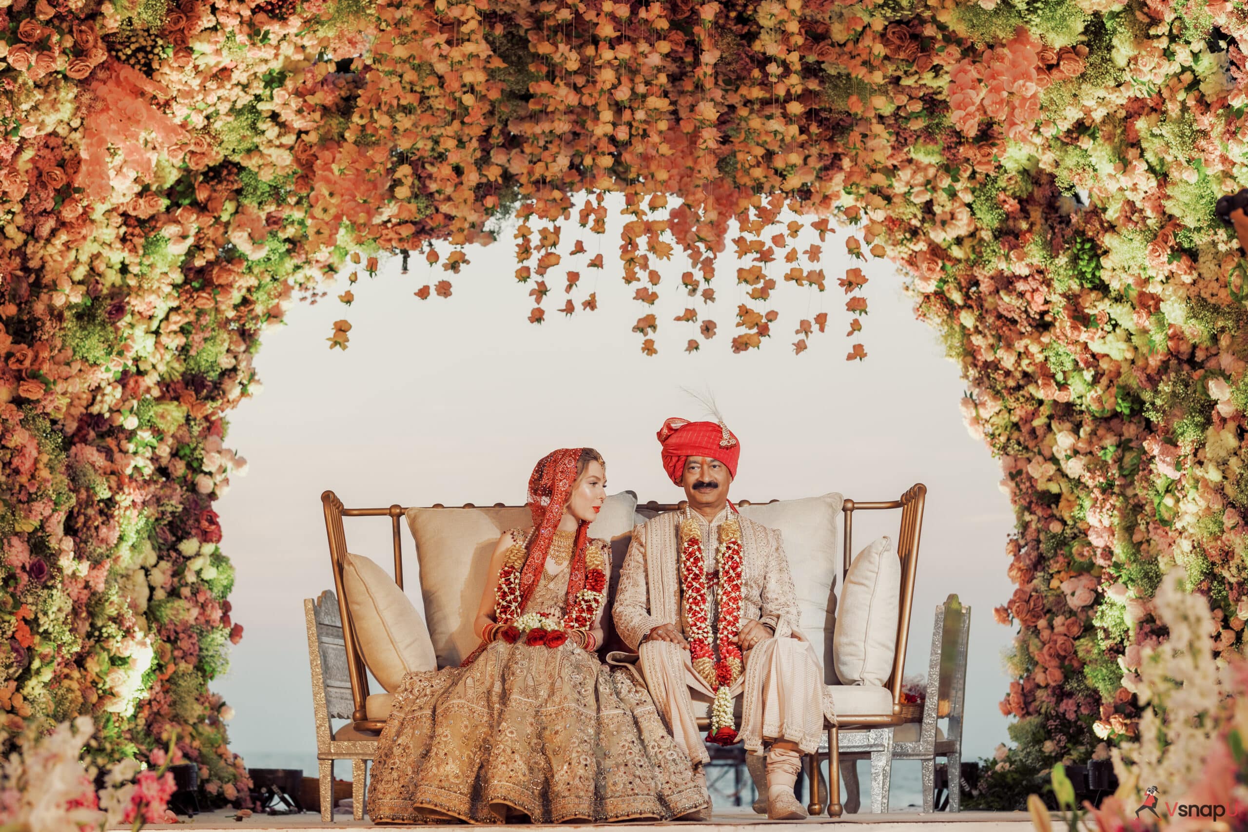 A stunning wedding scene with the bride and groom seated on a floral-themed stage.
