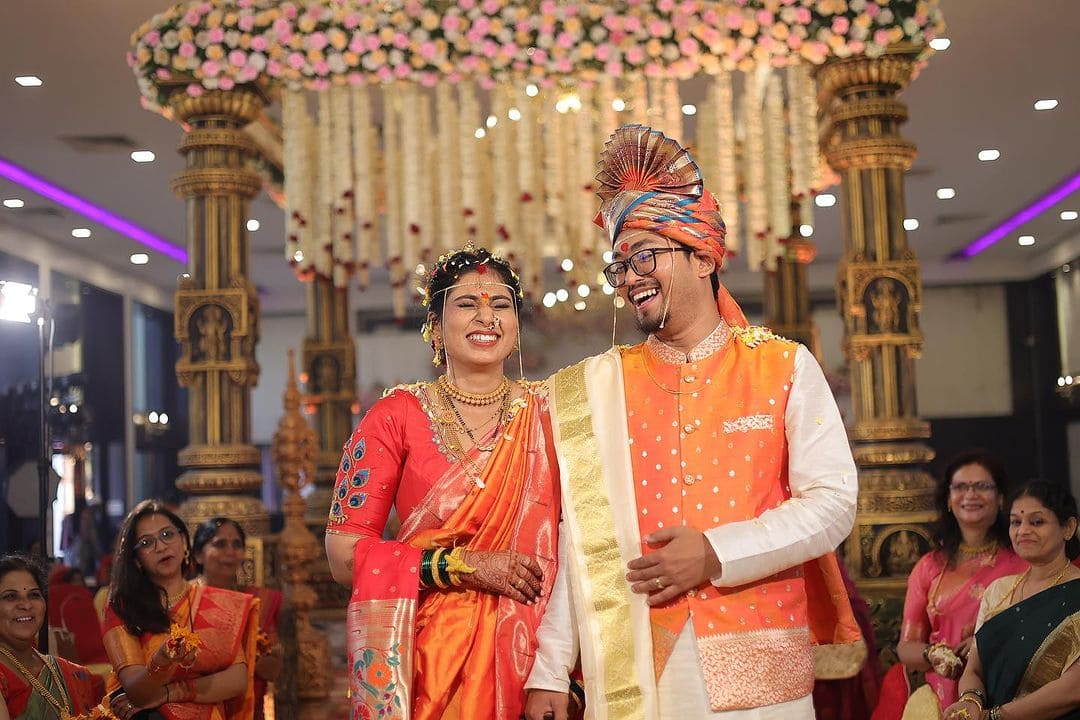 A romantic wedding moment as the groom stands, gazing at the bride in the mandap hall.