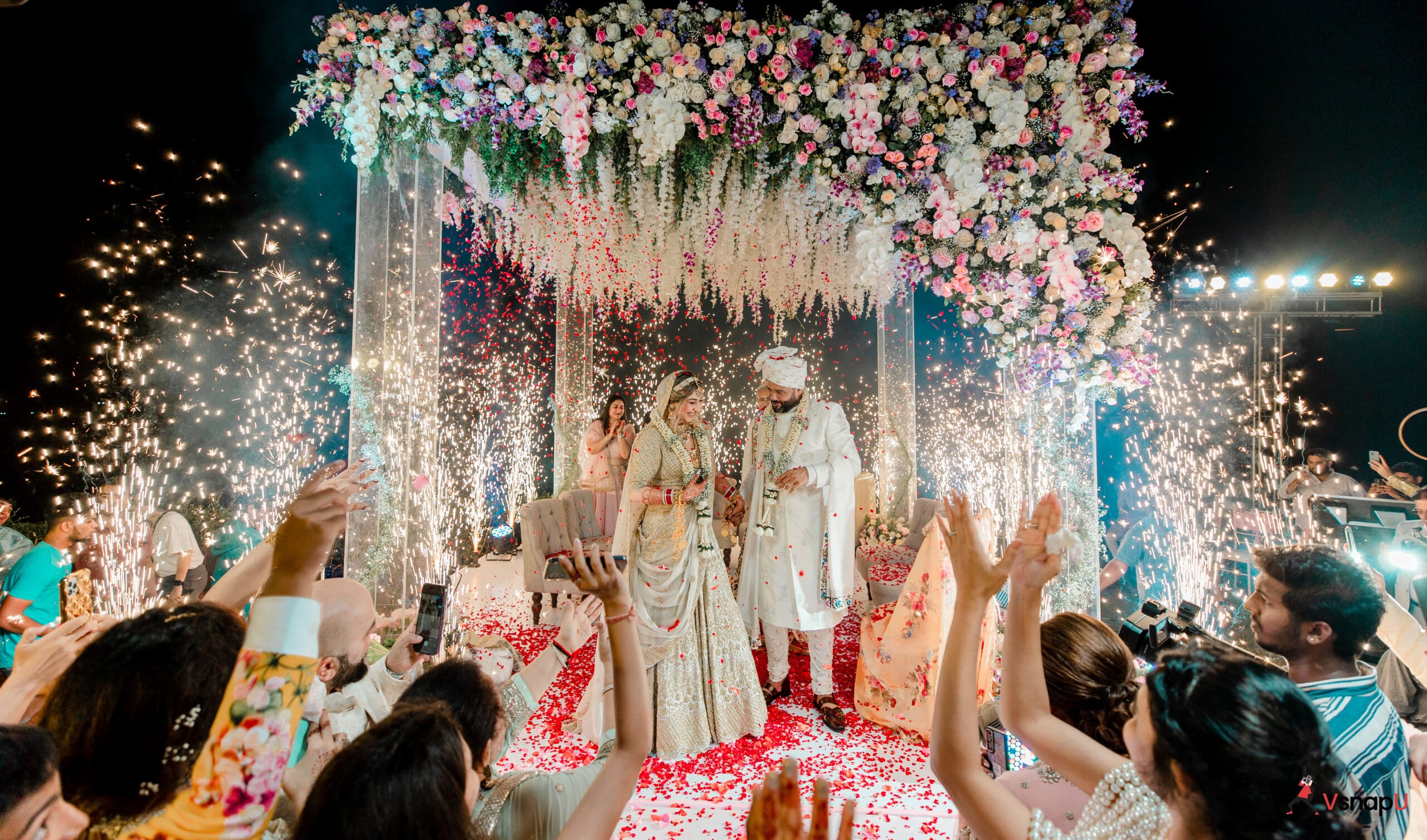 The groom and bride smile at each other, standing together on a floral stage, ready to begin their lifelong journey.